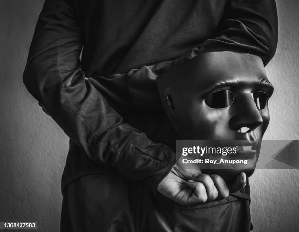 monochrome shot of mystery man holding and hide the hacker mask behind his back. - anonymous mask photos et images de collection