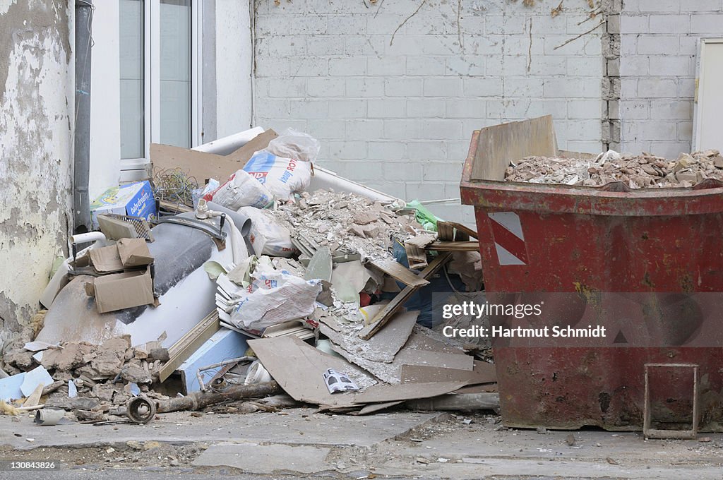 Tenement reconstruction, filled red skip, pile of debris on the side, new window at back