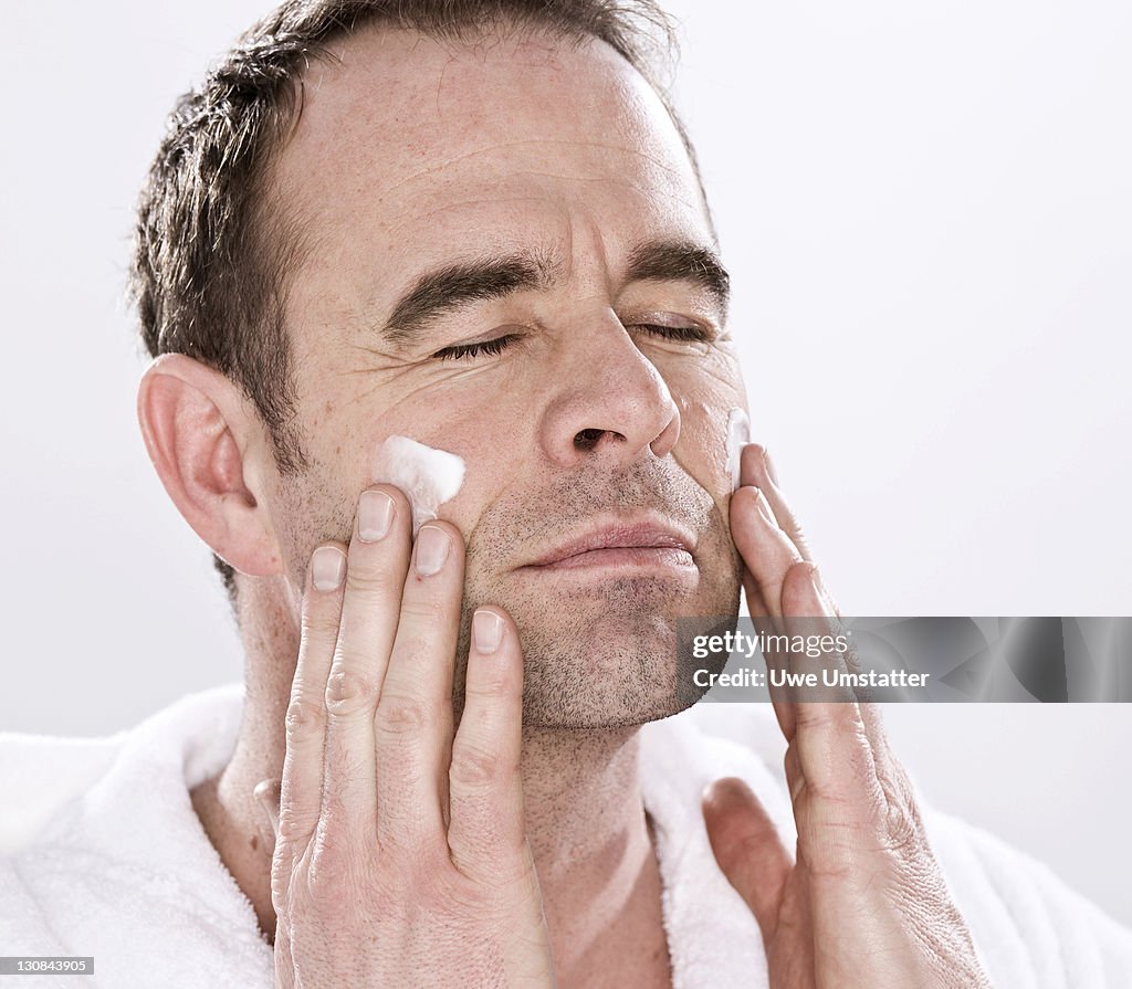 Man wearing a bathrobe, relaxed, putting lotion on his face
