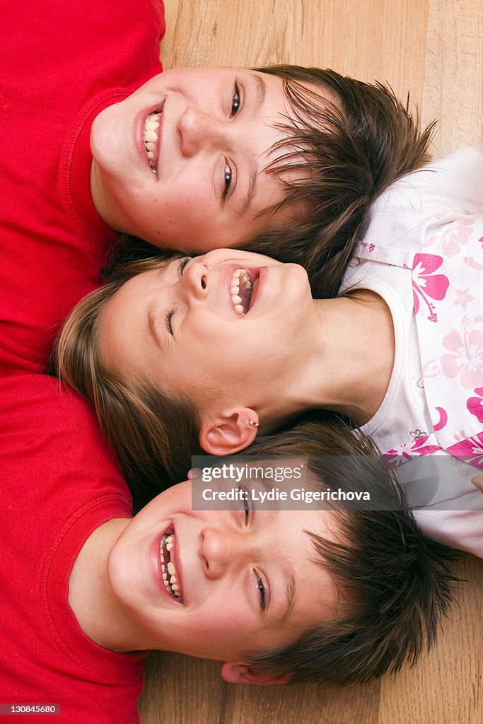 Girl, 4 years, and boys, 6 and 11 years, lying on the floor, laughing