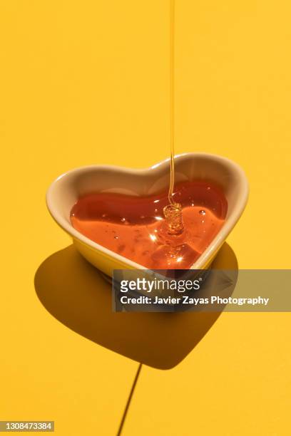 honey on a heart shaped bowl on yellow background - lipide foto e immagini stock