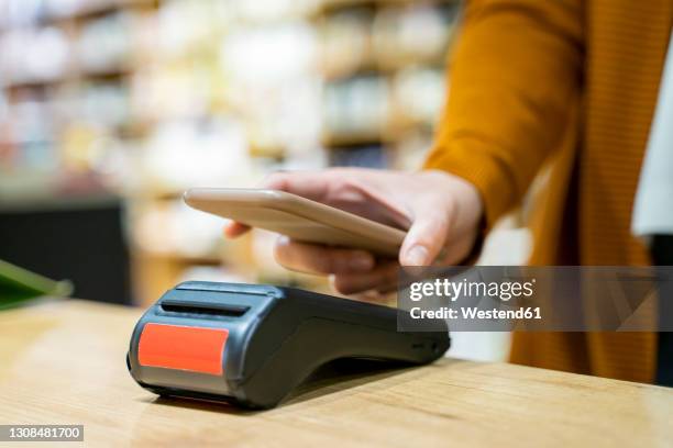 young woman paying at checkout of grocery store using smart phone - card reader stock pictures, royalty-free photos & images