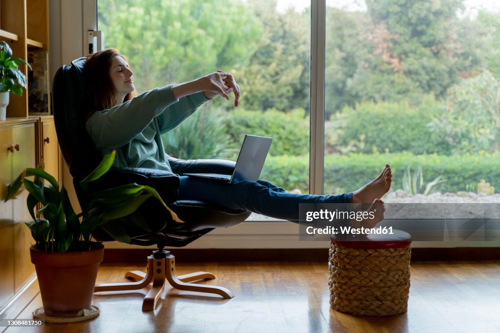 Mid adult woman stretching hand while sitting on chair at home