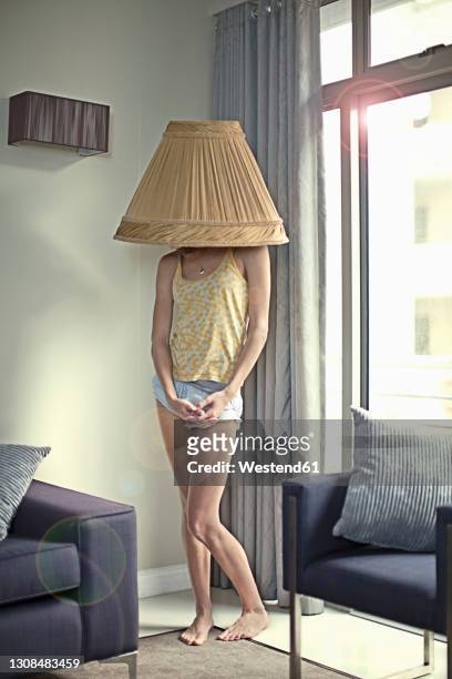 young woman with lamp shade on head standing at home - lamp shade fotografías e imágenes de stock