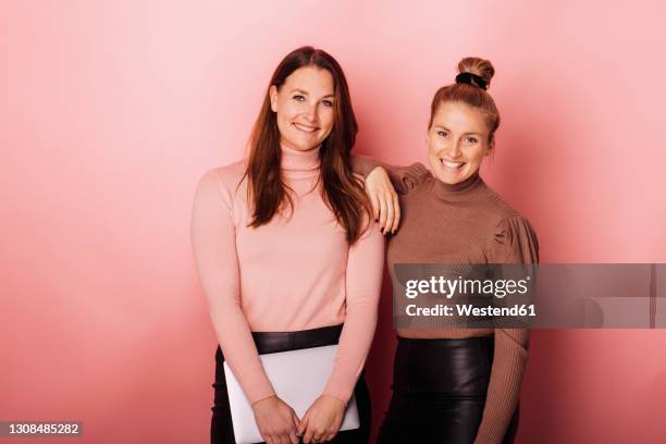 smiling businesswomen with laptop standing against peach background - two people portrait stock pictures, royalty-free photos & images