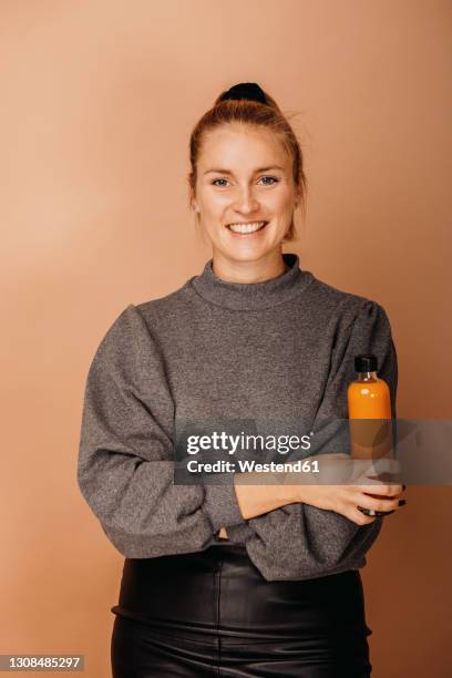 smiling businesswoman with arms crossed holding bottle of smoothie against brown background - blended drink ストックフォトと画像