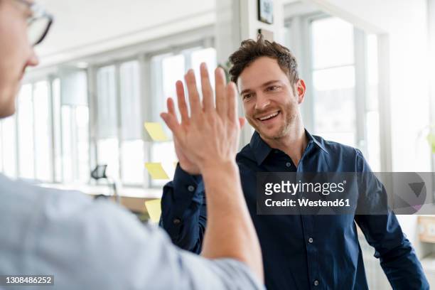 happy male colleagues doing high-five at office - hi five stockfoto's en -beelden
