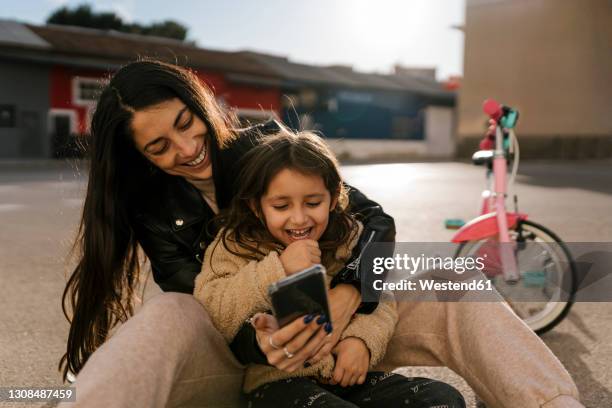 smiling mother using mobile phone while sitting on road - child phone stockfoto's en -beelden