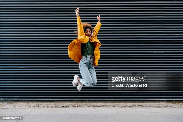 carefree woman with arms raised jumping against wall - jumping for joy stockfoto's en -beelden