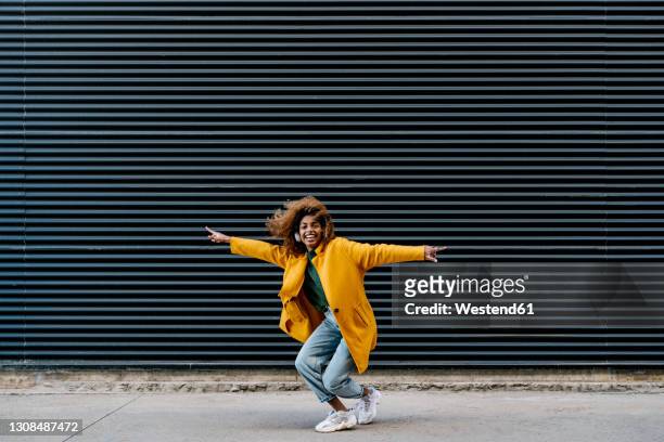cheerful afro woman with arms outstretched having fun against wall - frizzy hair stockfoto's en -beelden