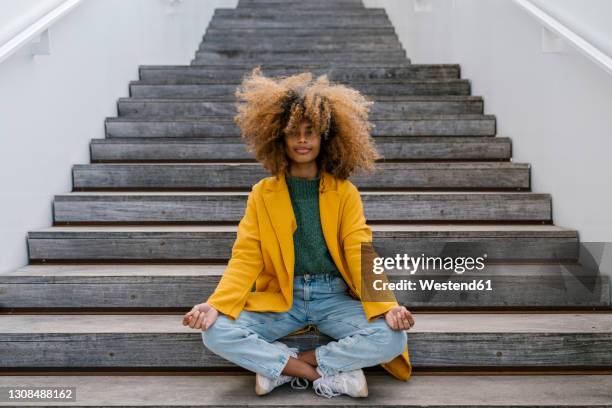 afro woman in lotus position sitting on staircase - frizzy hair foto e immagini stock