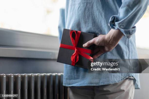 man holding gift box behind while standing at home - hiding behind back stock pictures, royalty-free photos & images