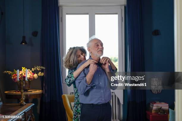 smiling woman adjusting bow tie of man while standing at home - senior getting dressed stock pictures, royalty-free photos & images