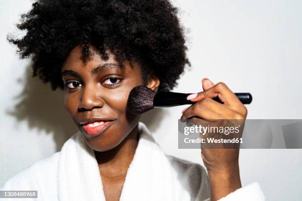 smiling woman using blushbrush while standing against white background - blush makeup ストックフォトと画像