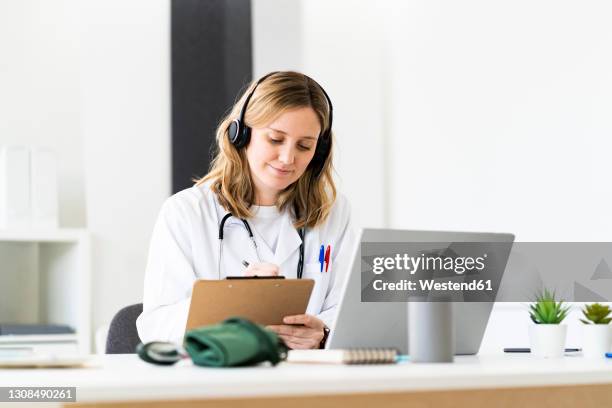 female medical worker writing on clipboard while giving online consultation through laptop in medical clinic - doctor using laptop stock pictures, royalty-free photos & images