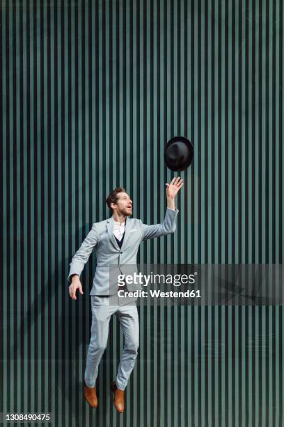 male professional jumping while throwing hat against wall - levitating foto e immagini stock