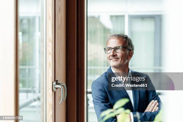 smiling male business professional looking through window in office - ビジネスフォーマル ストックフォトと画像
