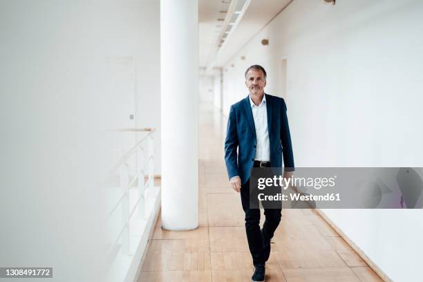 serious male entrepreneur walking in corridor at office - business man walk stock-fotos und bilder