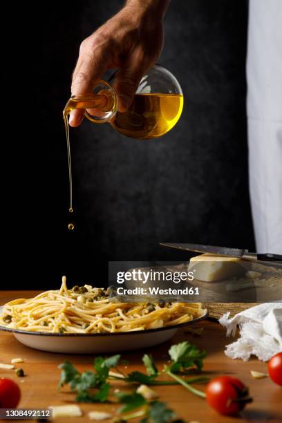 man pouring olive oil on spaghetti in plate - olive oil stock pictures, royalty-free photos & images