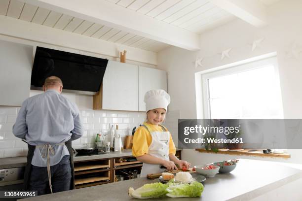 smiling girl cutting vegetable while standing in kitchen at home - schürze mann rückansicht stock-fotos und bilder