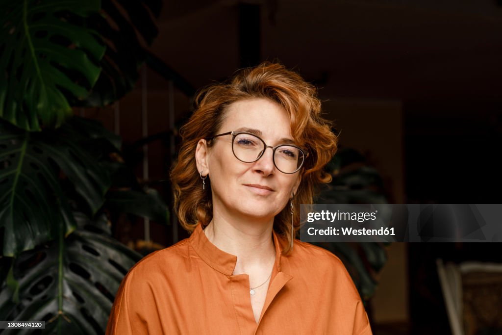 Confident mature woman with eyeglasses against plants at home