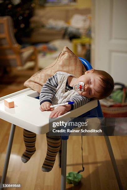 baby, 8 months, sleeping with pacifier in mouth and a pen in the hand in a child seat - pacifier stock pictures, royalty-free photos & images