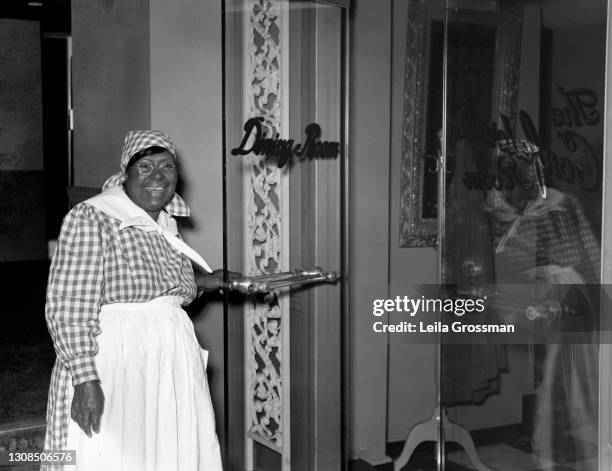View a waitress dressed as Aunt Jemima holding the door to the Confederate Room restaurant dining hall circa 1950 in Nashville, Tennessee.
