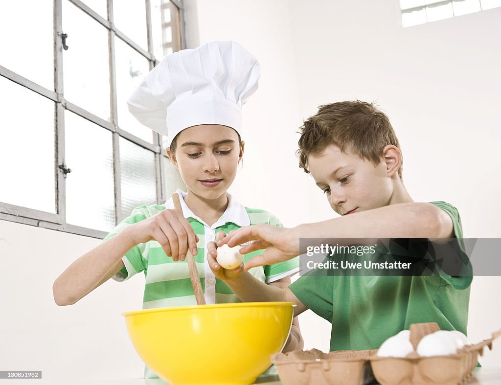 Girl wearing a chef's hat and a boy cracking eggs into a bowl