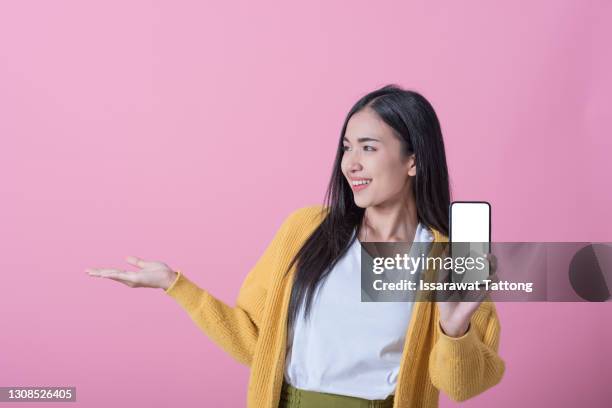 close up portrait of a smiling asian woman showing blank screen mobile phone while standing isolated over pink background - mobile advertising stock-fotos und bilder