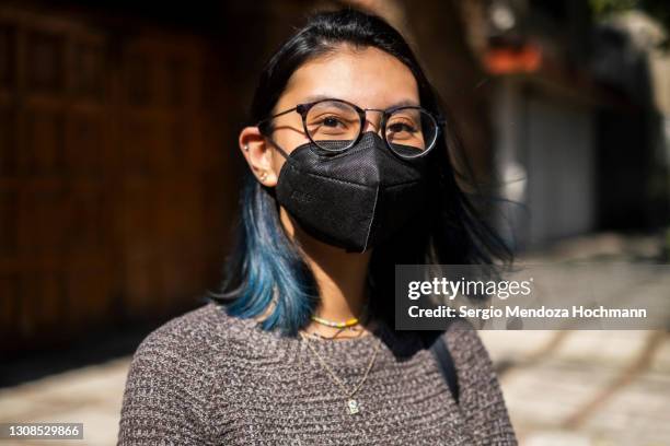 young latino woman wearing a face mask and looking at the camera on a sunny day - mascarilla-n95 fotografías e imágenes de stock