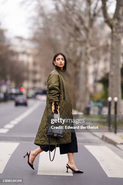 Melanie Darmon wears a green khaki long quilted padded puff winter coat from Aigle, a black yellow and white floral print shirt from Versace, black...