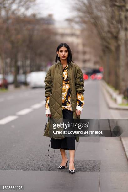 Melanie Darmon wears a green khaki long quilted padded puff winter coat from Aigle, a black yellow and white floral print shirt from Versace, black...