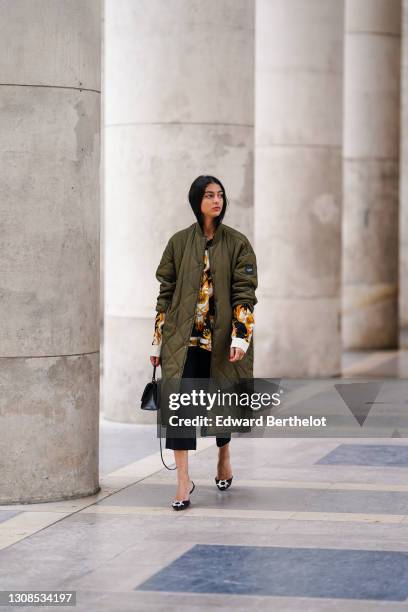 Melanie Darmon wears a green khaki long quilted padded puff winter coat from Aigle, a black yellow and white floral print shirt from Versace, black...
