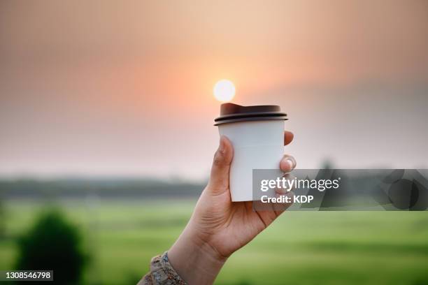 close-up of woman hand holding a cup of coffee made from bio plastic against with agricultural fields rural scene during sunrise background. - personal perspective coffee stock pictures, royalty-free photos & images