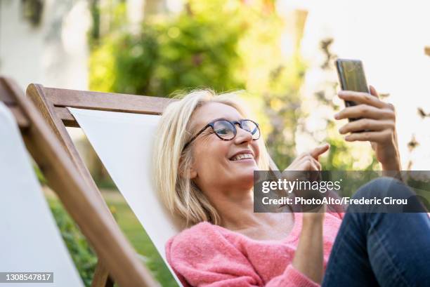 smiling mature woman using smartphone while sitting on deckchair - 50 54 jahre stock-fotos und bilder