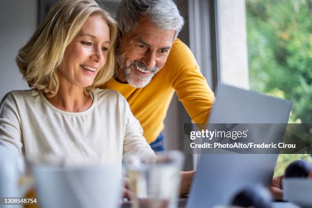 smiling mature couple using laptop at home - 55 couple ストックフォトと画像