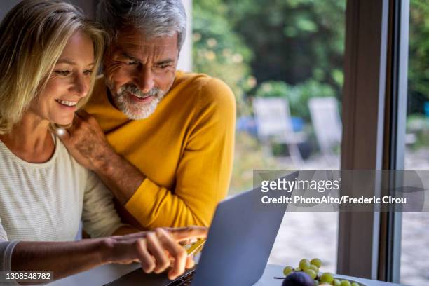 smiling mature couple making online payment with credit card - couple 50 55 laptop stock-fotos und bilder