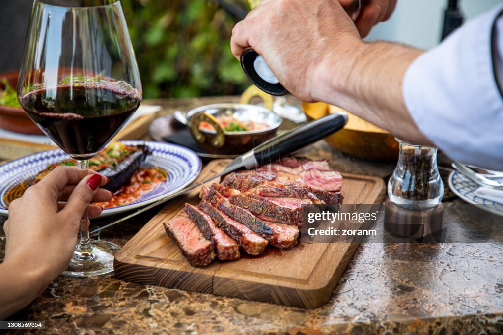 Tempere bife médio raro com moedor de sal, cortado em tábua de madeira na mesa do restaurante