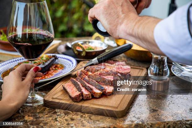 seasoning medium rare steak with salt grinder, cut on wooden board on restaurant table - steak imagens e fotografias de stock