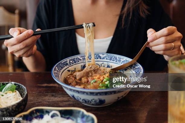 cropped shot of young woman eating chinese noodle soup in restaurant - nouilles photos et images de collection