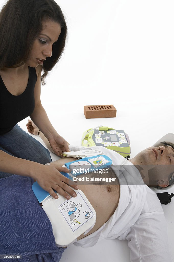 Woman resuscitating a man using a defibrillator
