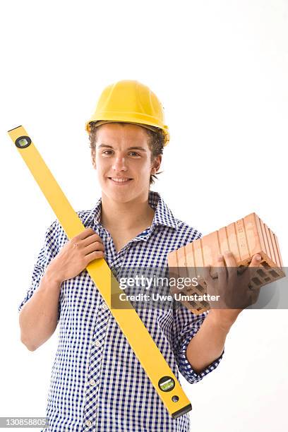 trainee wearing a hard hat, with a water level and a brick - boy in hard hat photos et images de collection