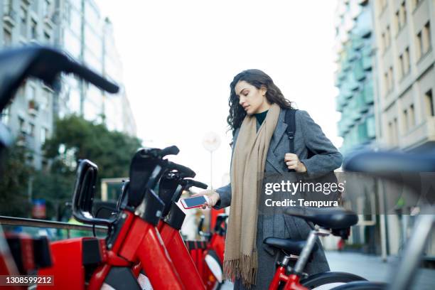 een jonge vrouw die een app gebruikt om een gedeelde fiets te huren. - bicycle rental stockfoto's en -beelden