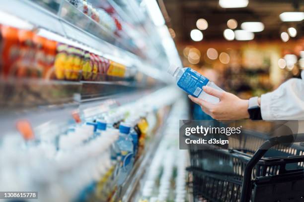 close up of woman with shopping cart shopping for a bottle of healthy beverage from refrigerated shelves in a supermarket. healthy eating lifestyle - コンビニ ストックフォトと画像