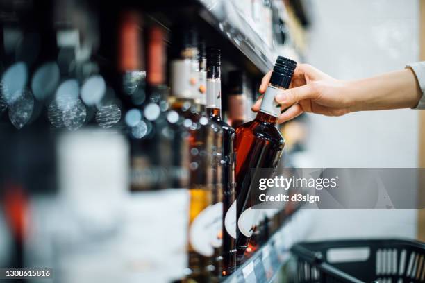 close up of woman walking through liquor aisle and choosing a bottle of liquor from the shelf in a supermarket - buying alcohol stock pictures, royalty-free photos & images