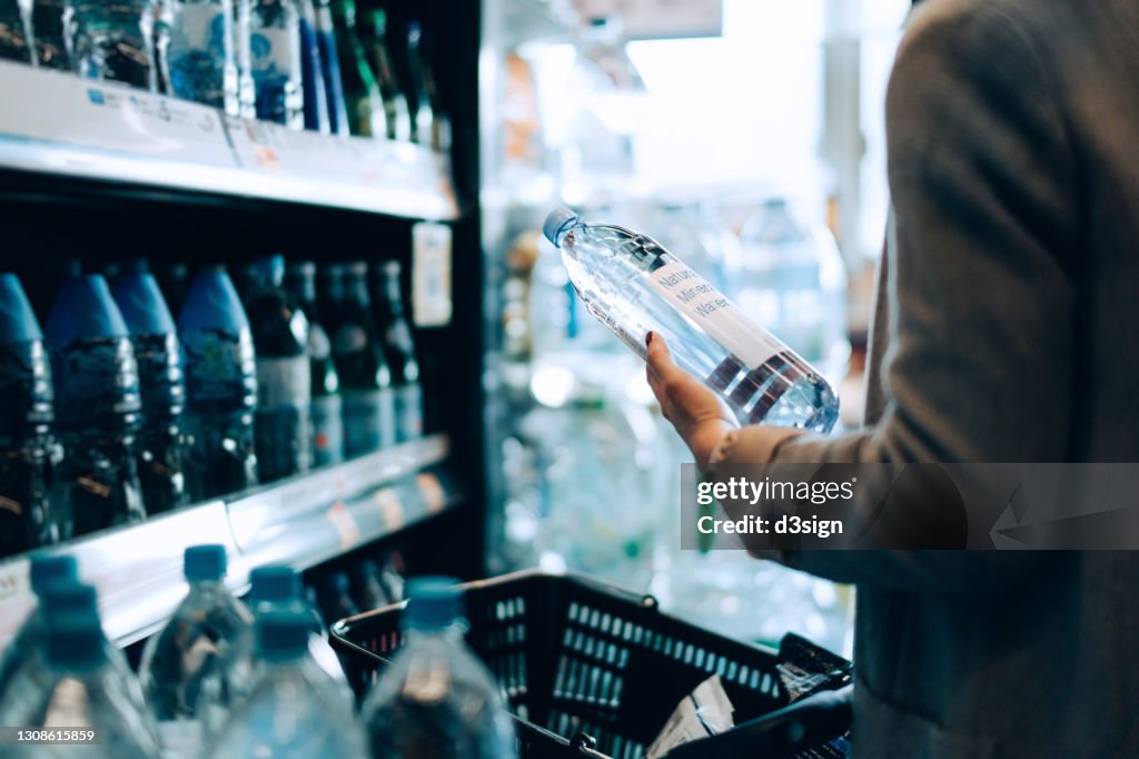 Close up of woman with shopping cart shopping for bottled water along the beverage aisle in a supermarket. Healthy eating lifestyle