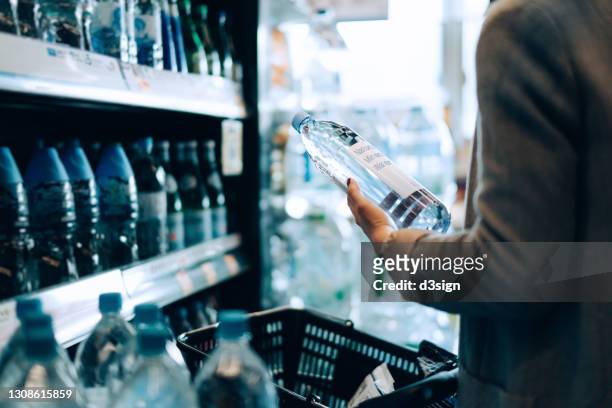 close up of woman with shopping cart shopping for bottled water along the beverage aisle in a supermarket. healthy eating lifestyle - garrafa de água garrafa imagens e fotografias de stock