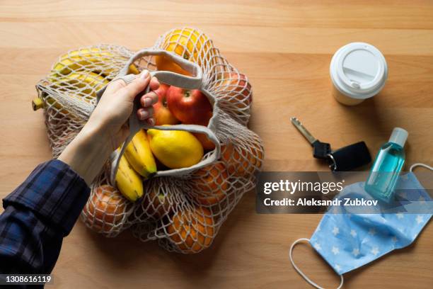 reusable protective mask, hand sanitizer, car keys, coffee mug to take away. a woman puts, takes or holds an eco-bag or string bag with organic farm products or purchases. preventing the spread of the covid-19 virus. a way of life in a pandemic. - car keys table stock pictures, royalty-free photos & images