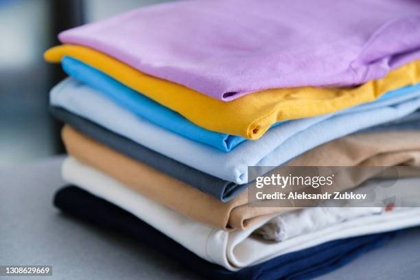 a stack of things on a gray background, in the room. clean folded cotton denim and bright colored t-shirts. the concept of housework, ironing, care and storage of things. a copy of the text space. - multi colored shirt foto e immagini stock