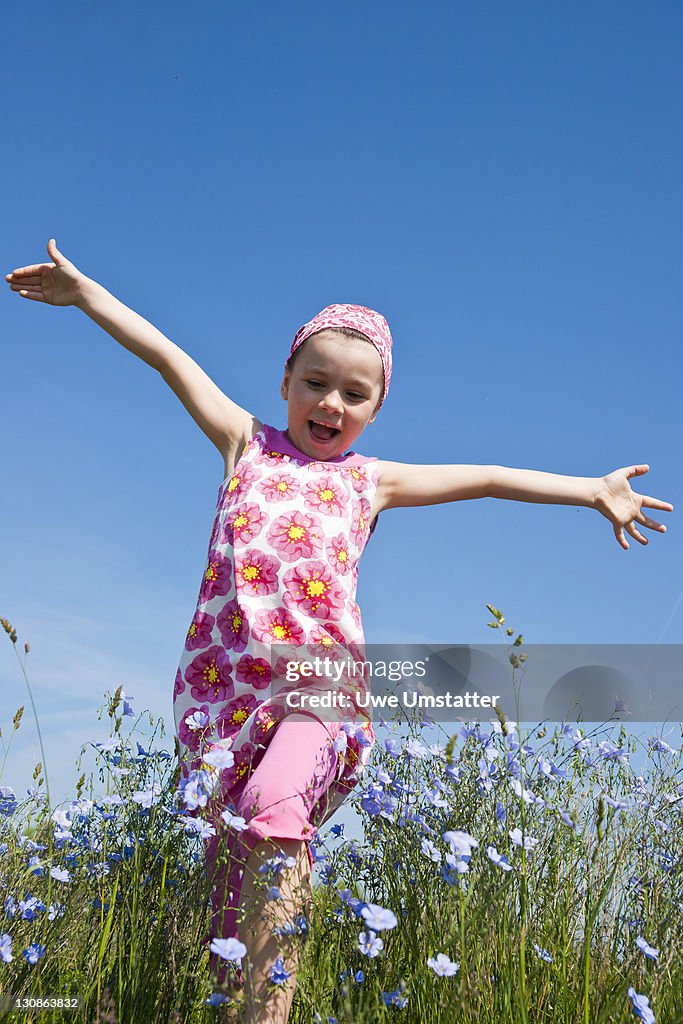 Laughing girl running across a flower meadow